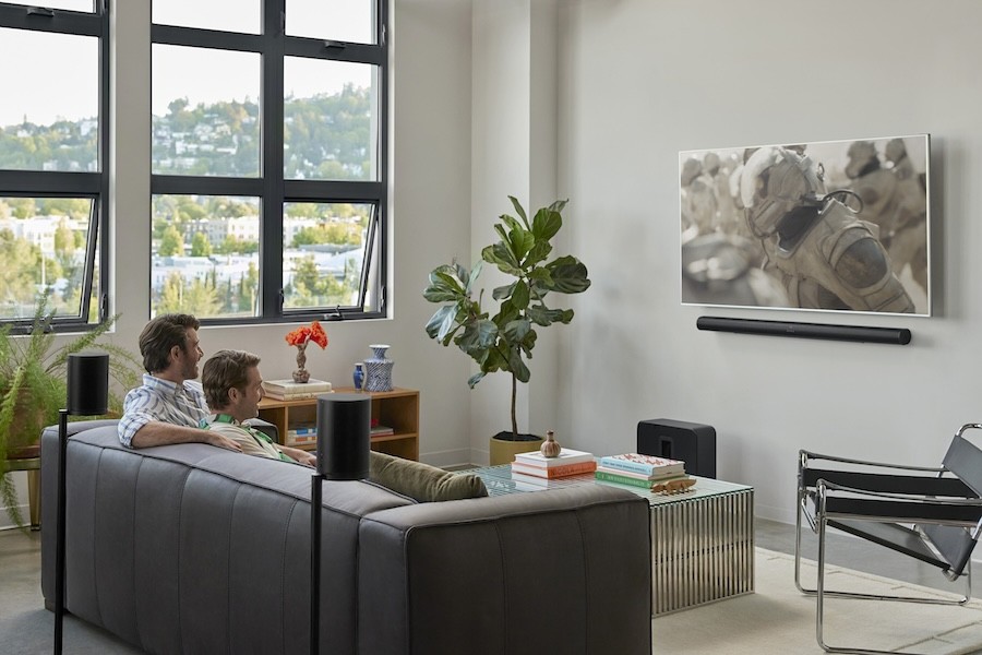 People sit on a couch watching a TV with a Sonos Arc Ultra mounted beneath it. A Sub 4 subwoofer sits on the floor.