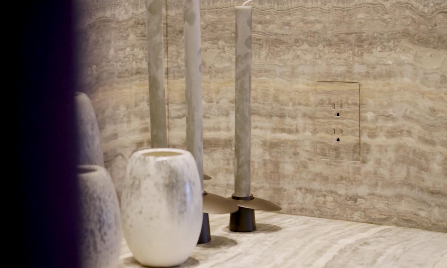 Close-up of a textured stone wall with sleek, minimalist electrical outlets and decorative candles.