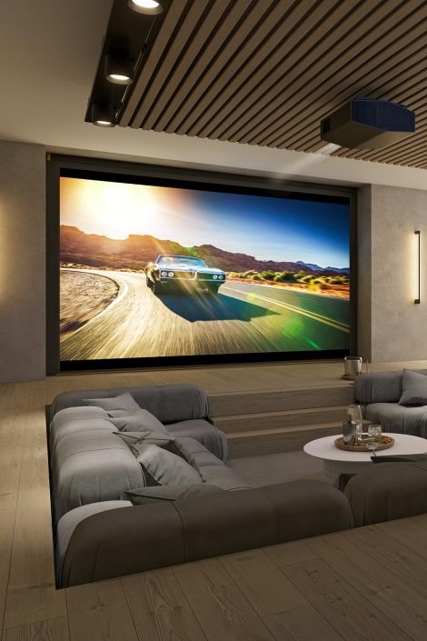 A home theater with tiered seating, a large screen showing a car racing scene, and warm lighting.