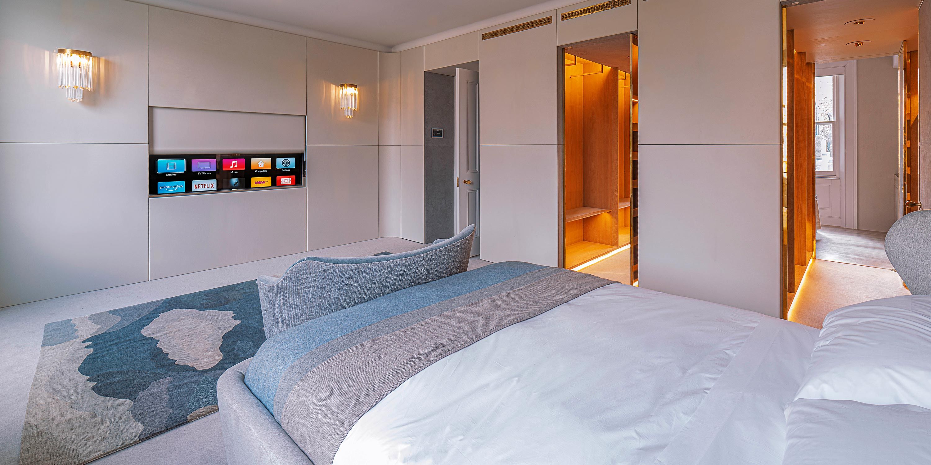 A modern bedroom featuring a sleek built-in entertainment display and luxurious lighting.