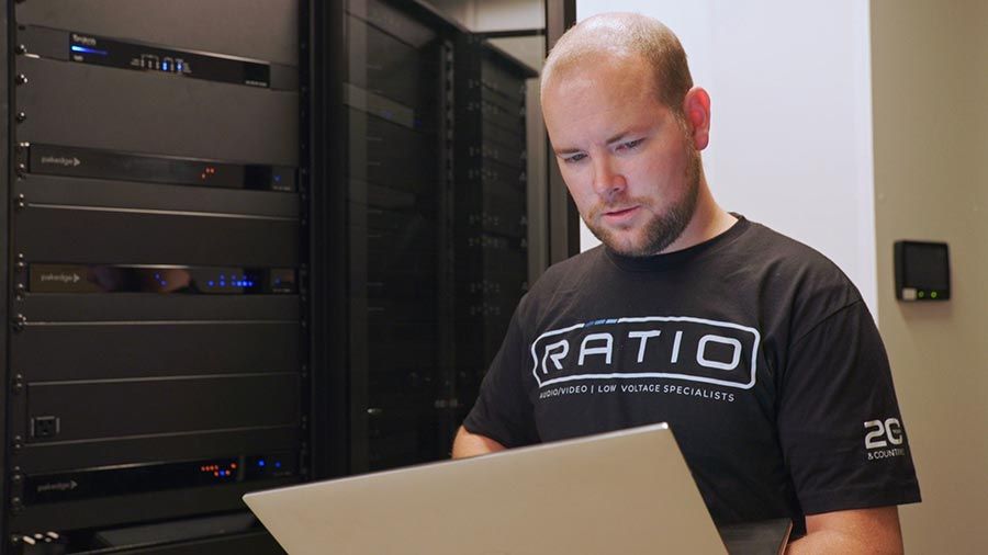 A technician working on a laptop in a server room filled with electronic equipment.