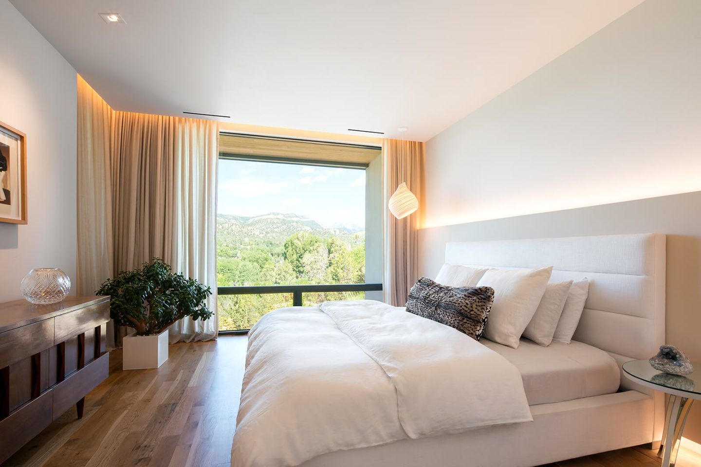 A cozy bedroom with large windows and warm ambient lighting.