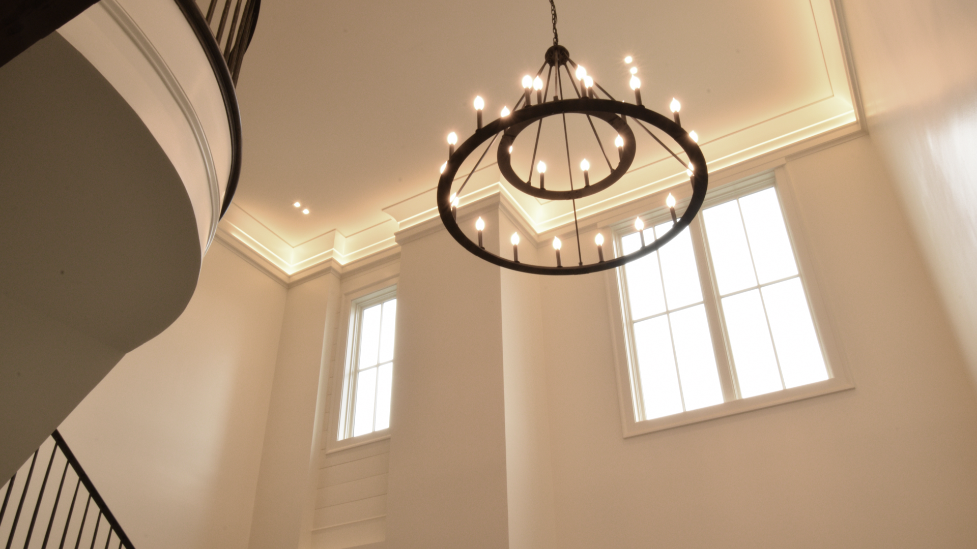 A stylish chandelier hanging in a high-ceilinged foyer with natural lighting.