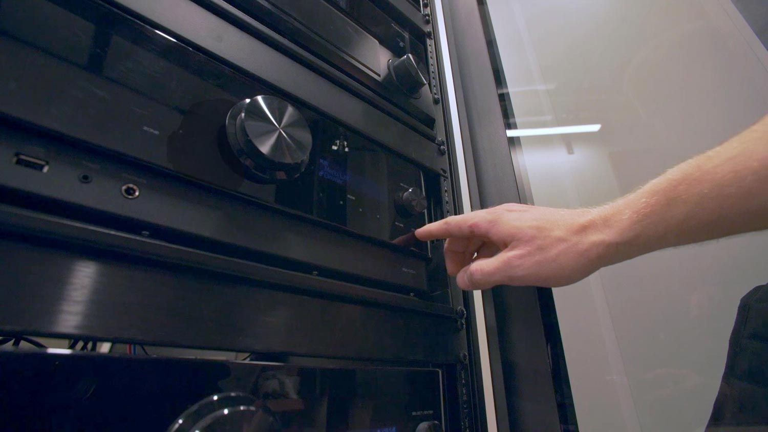 A hand adjusting settings on a sleek black AV equipment rack in a modern setup.