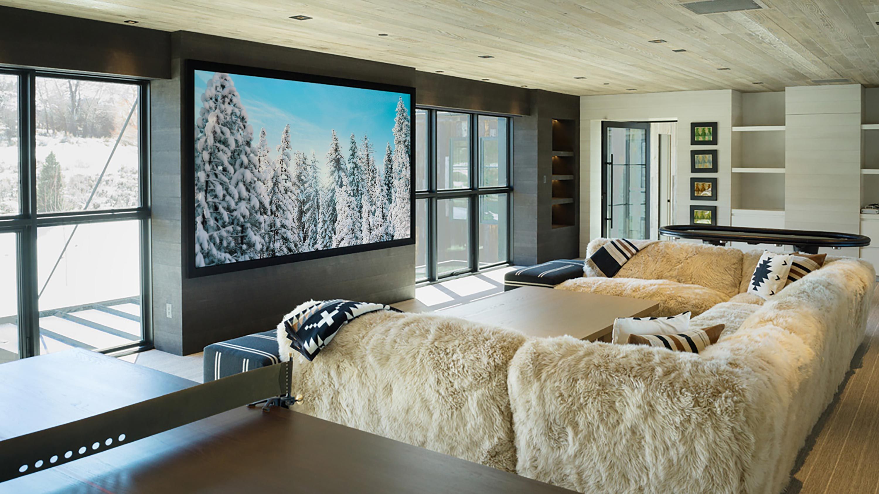 A media room with fur-lined sofas, a large wall-mounted screen, and expansive windows.